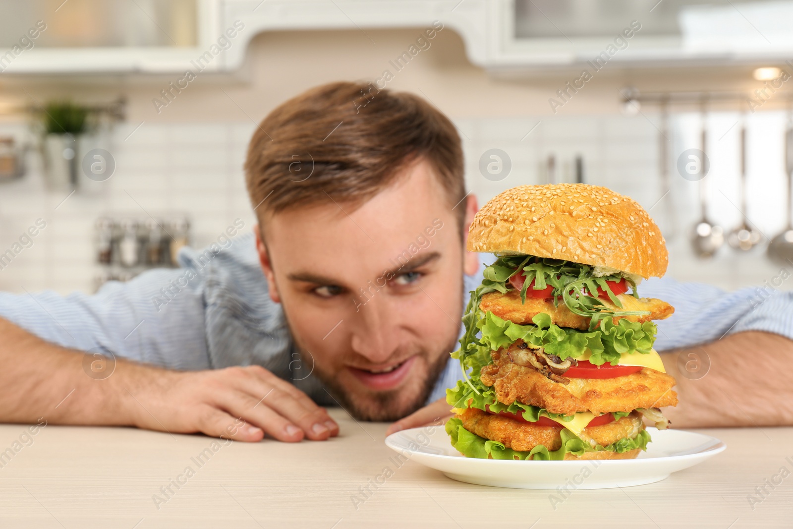 Photo of Young hungry man and huge burger on table