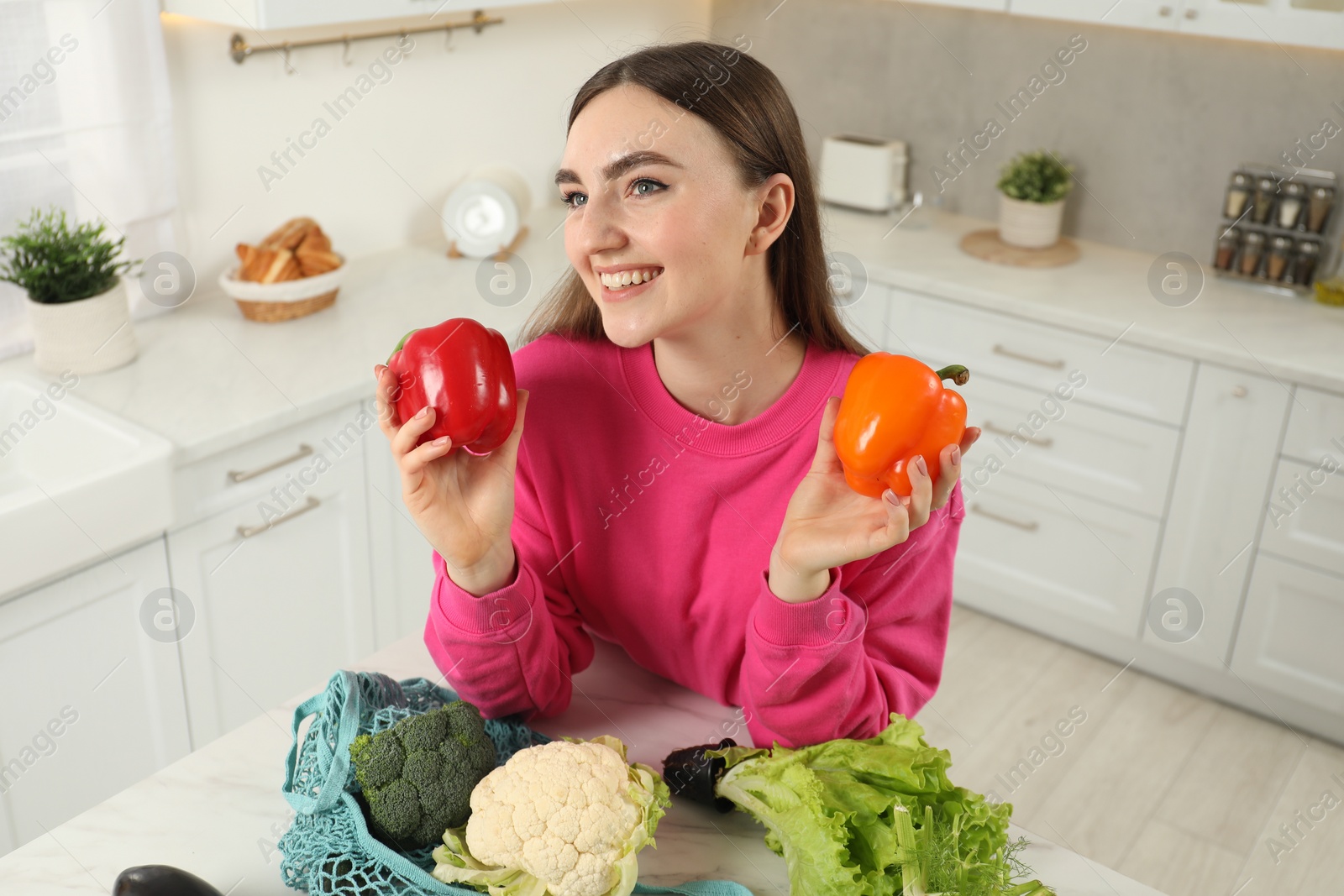 Photo of Woman with peppers and string bag of vegetables at light marble table in kitchen, above view