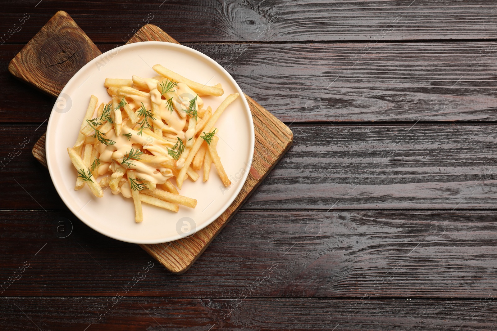 Photo of Delicious french fries with cheese sauce and dill on wooden table, top view. Space for text