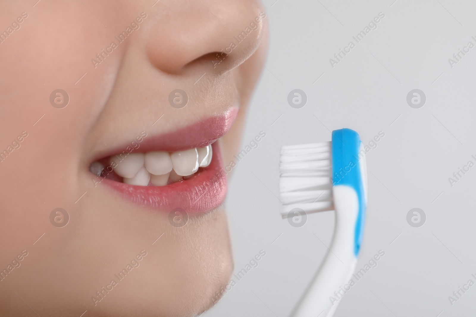 Photo of Girl brushing her teeth with toothbrush on light grey background, closeup