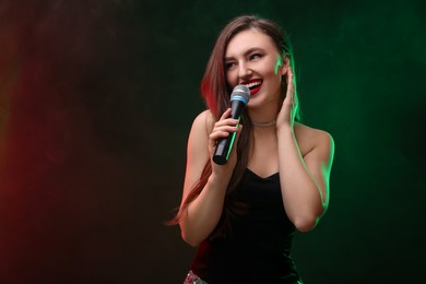 Photo of Beautiful woman with microphone singing in color lights on dark background. Space for text