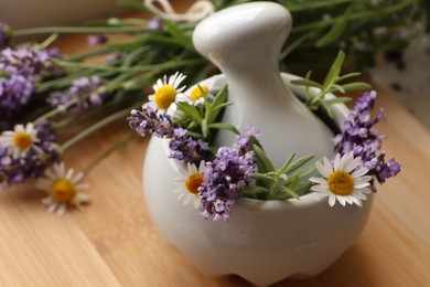 Mortar with fresh lavender, chamomile flowers, rosemary and pestle on wooden table