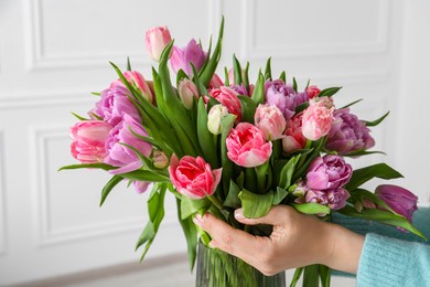 Photo of Woman putting bouquet of beautiful tulips in vase indoors, closeup