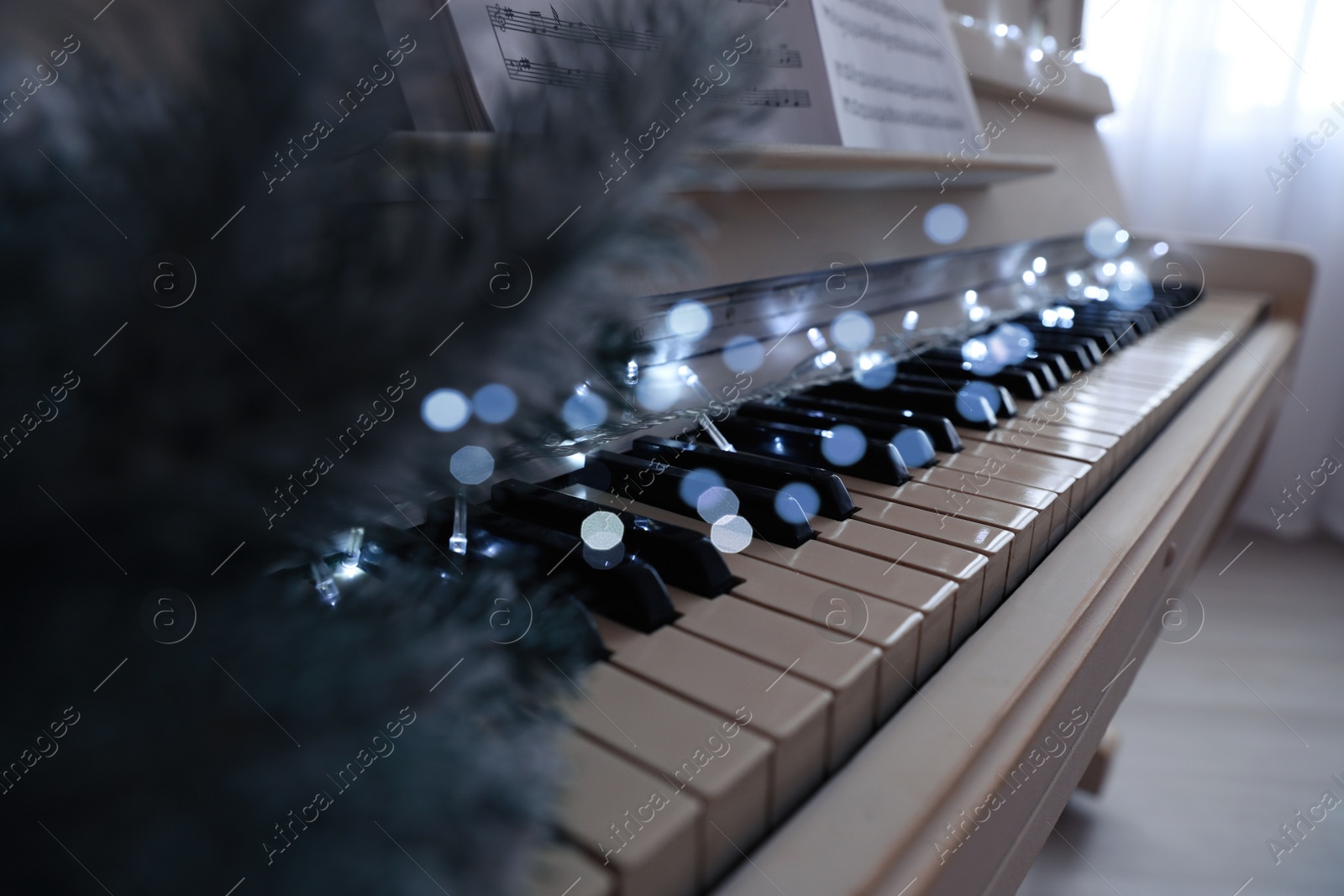 Photo of Glowing fairy lights on piano keys indoors, closeup. Christmas music