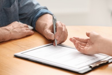 Notary showing senior man where to sign Last Will and Testament at wooden table indoors, closeup