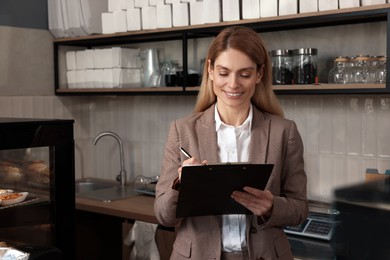 Happy business owner with clipboard and pen in bakery shop