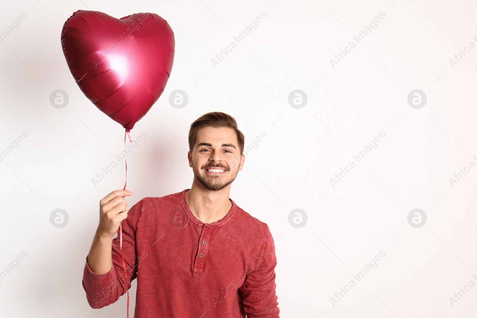 Photo of Portrait of young man with heart shaped balloon on white background. Space for text