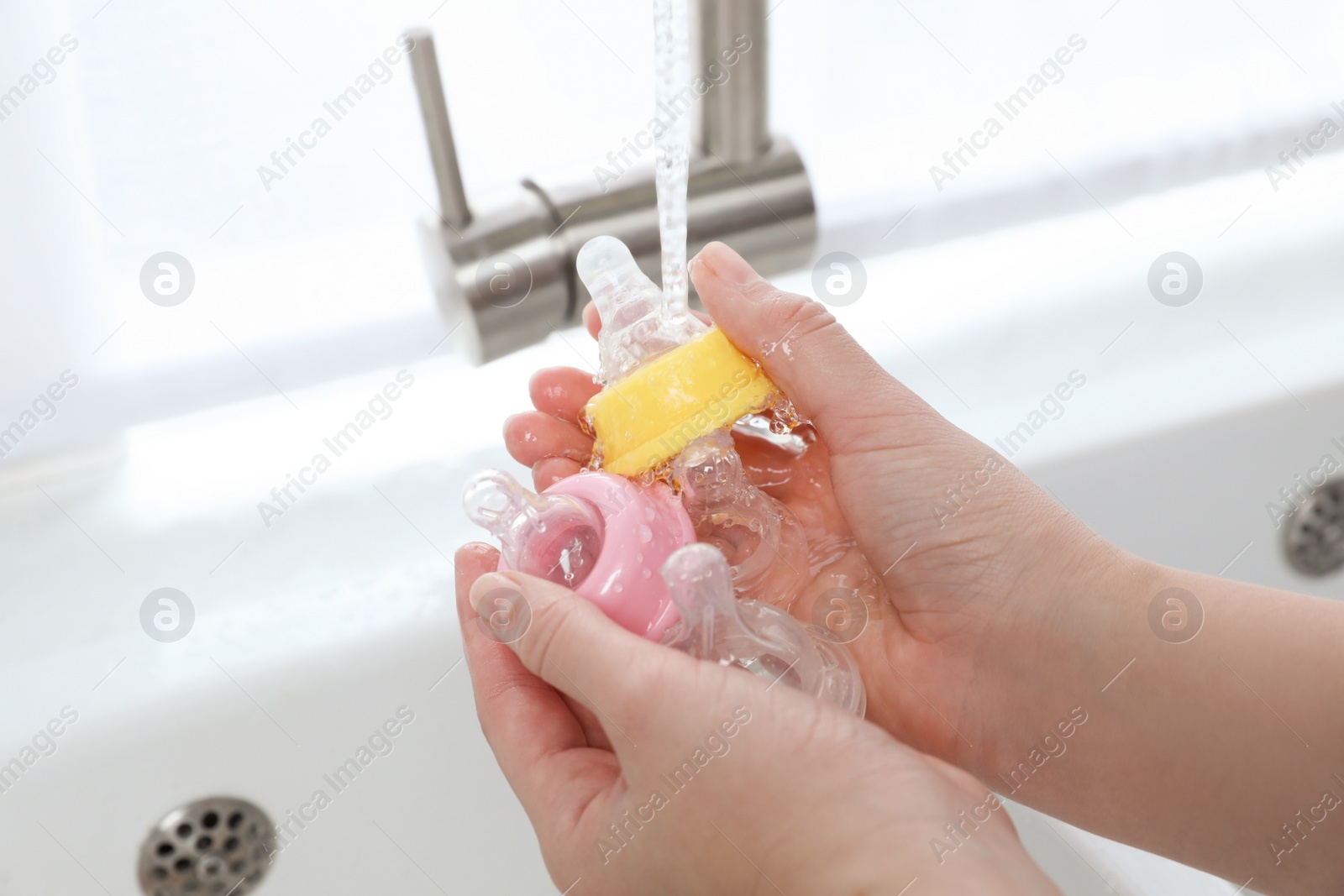 Photo of Woman washing baby bottle nipples under stream of water, closeup