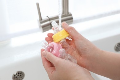 Photo of Woman washing baby bottle nipples under stream of water, closeup