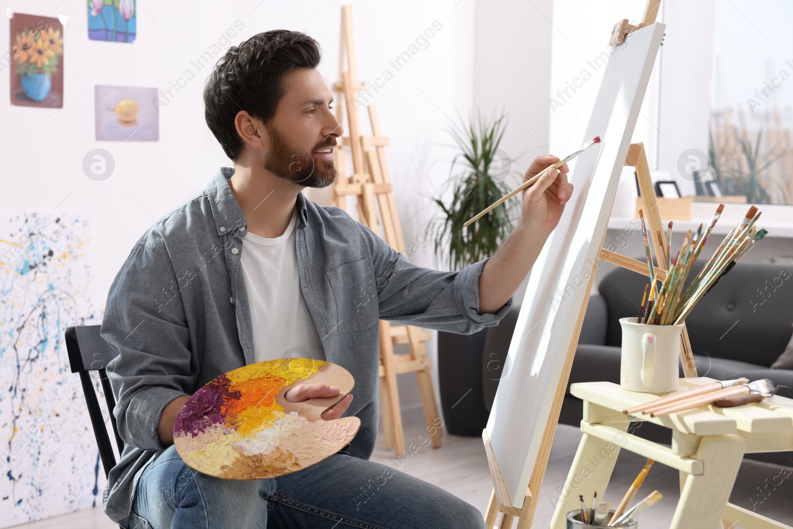 Photo of Man painting in studio. Using easel to hold canvas