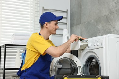 Smiling plumber with screwdriver repairing washing machine in bathroom