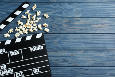 Photo of Clapper board and popcorn on blue wooden background, top view with space for text. Visiting cinema