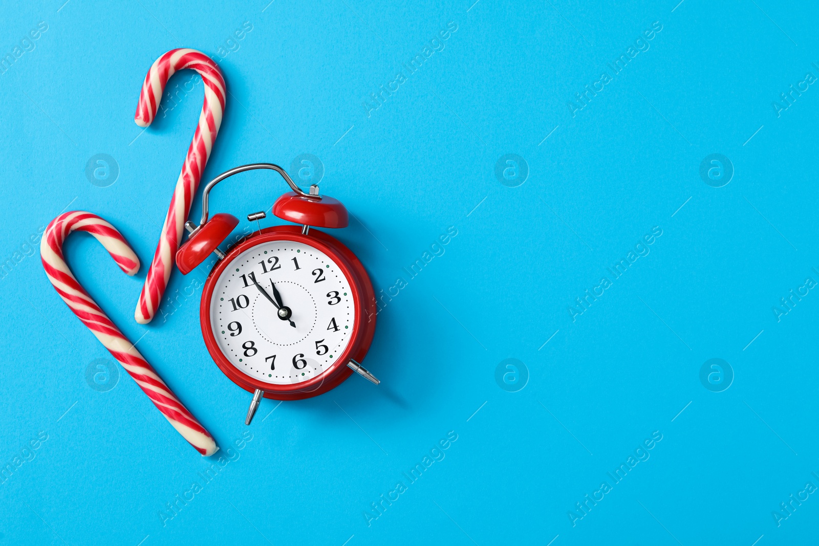 Photo of Alarm clock and candy canes on light blue background, flat lay with space for text. New Year countdown