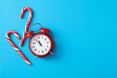 Photo of Alarm clock and candy canes on light blue background, flat lay with space for text. New Year countdown