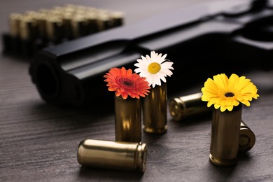 Beautiful blooming flowers, bullets and handgun on wooden table, closeup. Peace instead of war