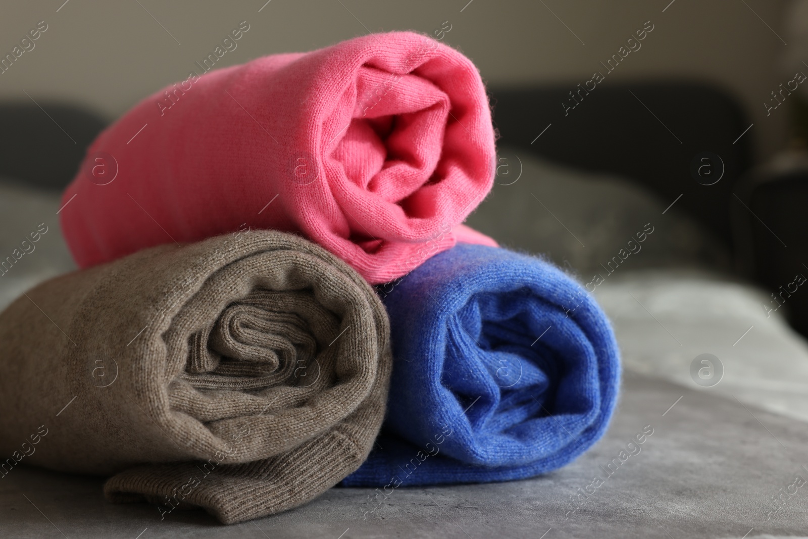 Photo of Rolled color sweaters on gray table, closeup