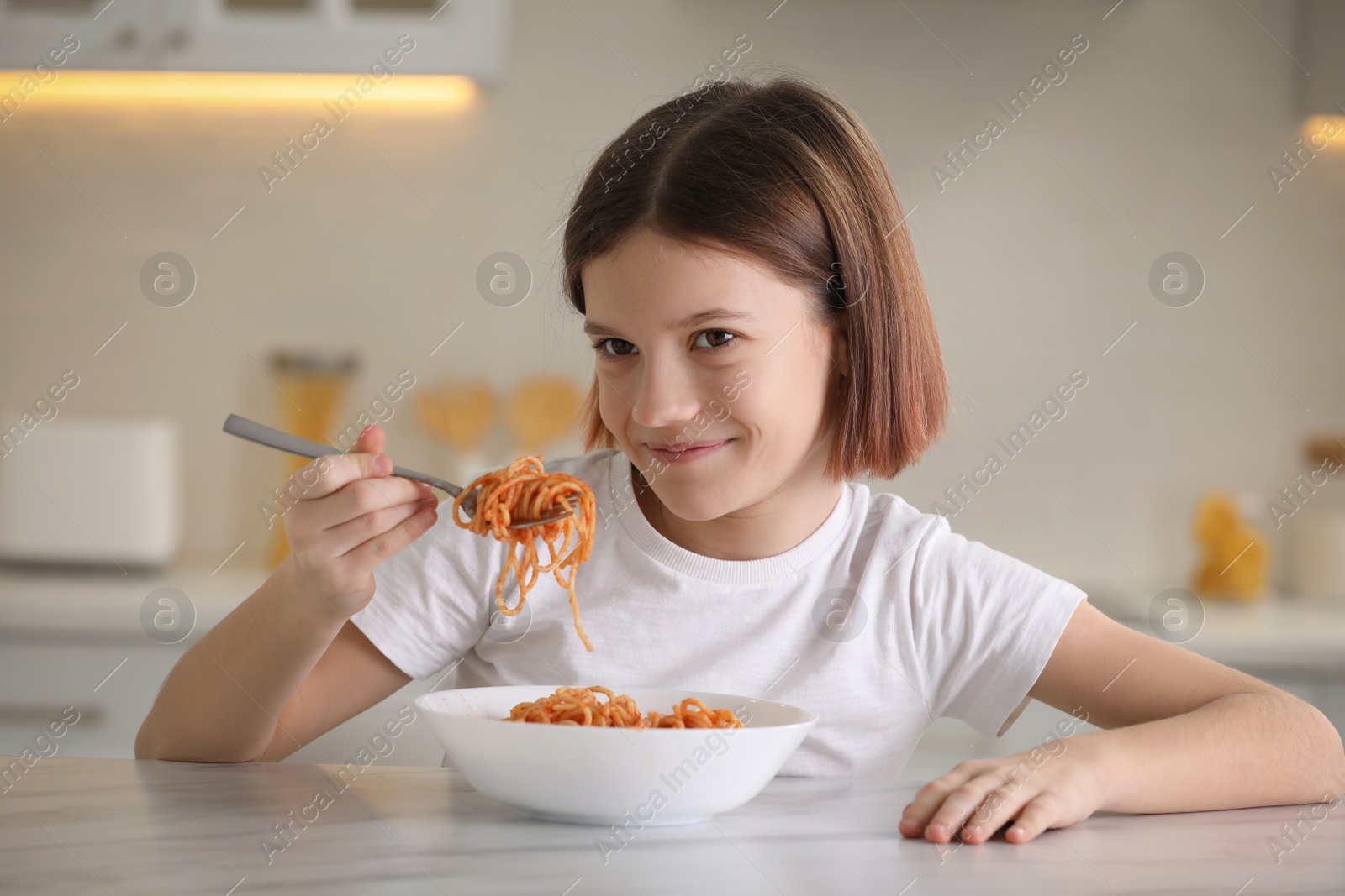 Photo of Happy girl eating tasty pasta at table in kitchen