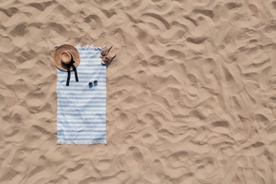 Image of Towel with beach accessories on sand, top view. Space for text