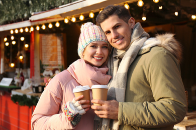 Photo of Happy couple in warm clothes with drinks at winter fair. Christmas season