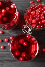 Photo of Tasty cranberry juice in glasses and fresh berries on black wooden table, flat lay