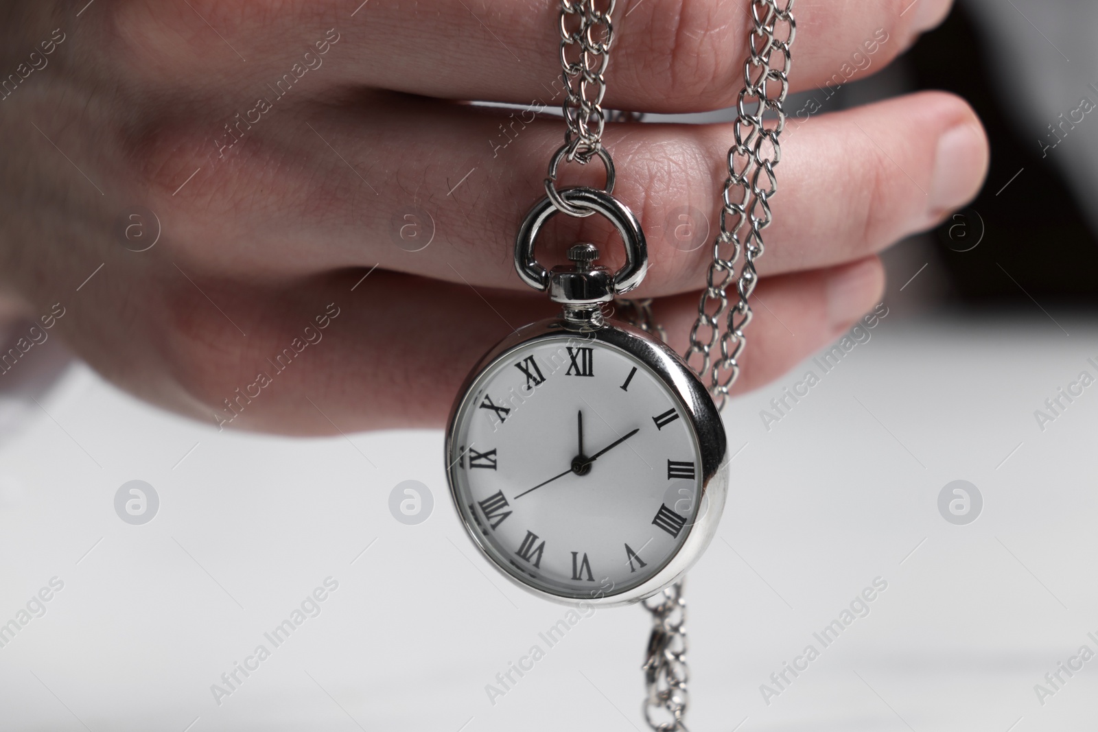 Photo of Man holding chain with elegant pocket watch at white table, closeup