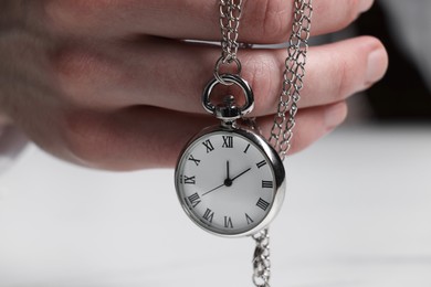 Man holding chain with elegant pocket watch at white table, closeup