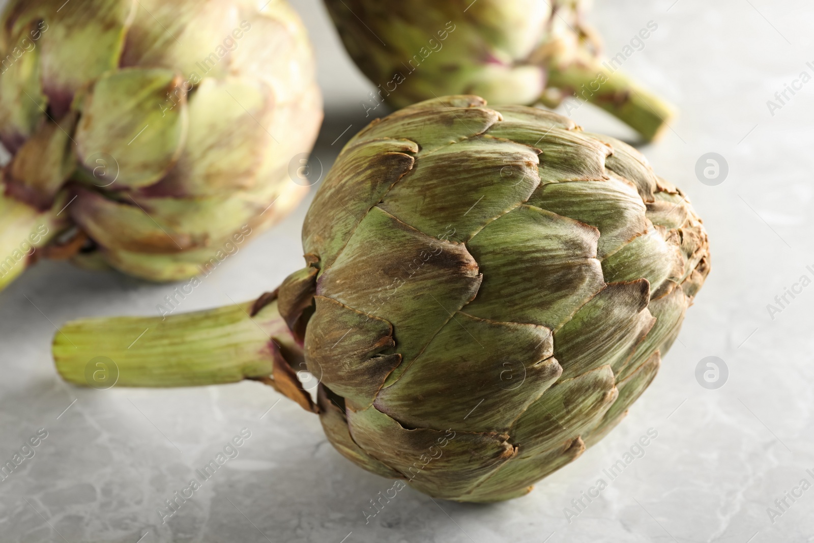 Photo of Fresh raw artichokes on grey marble table, closeup