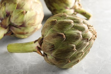 Photo of Fresh raw artichokes on grey marble table, closeup