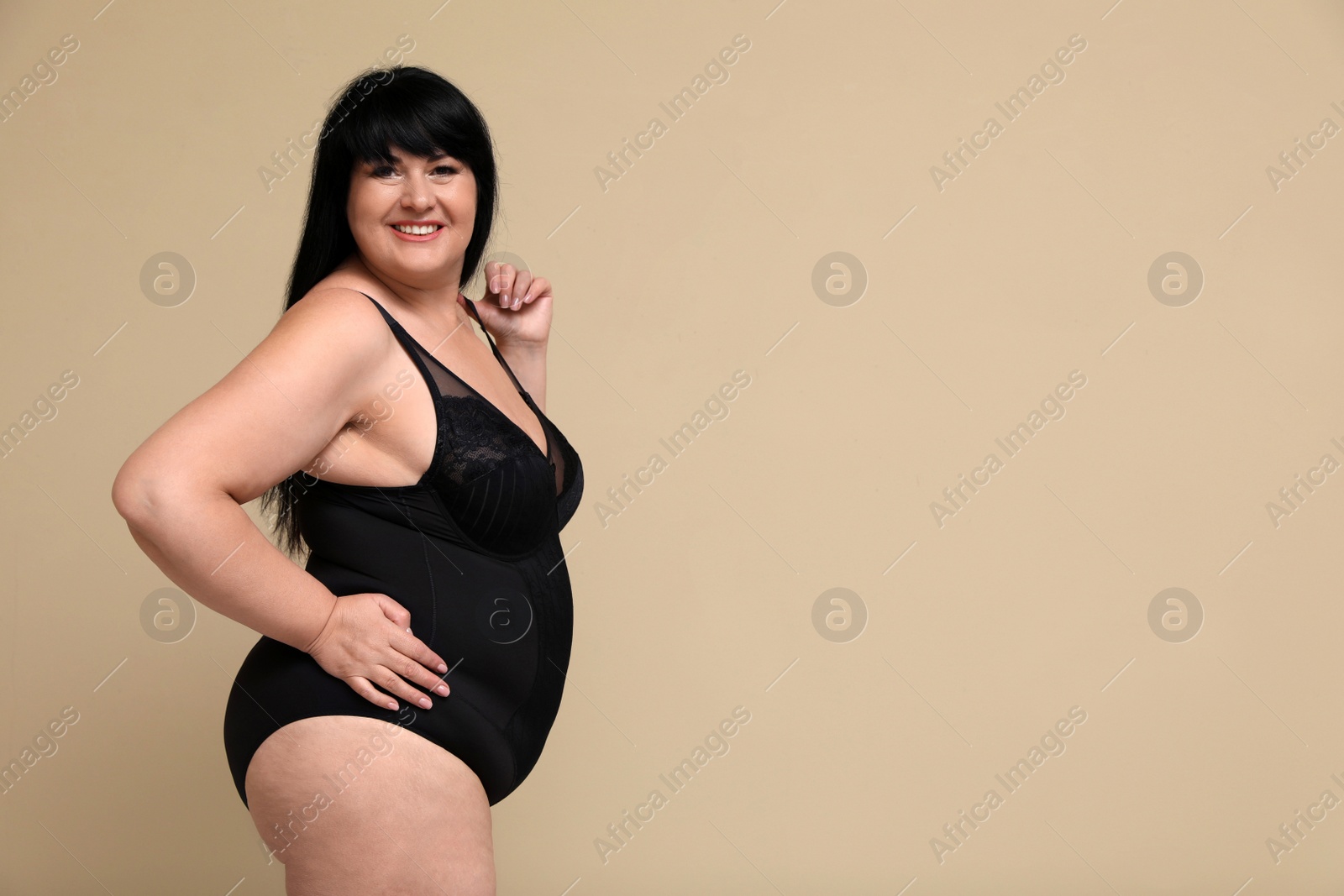 Photo of Beautiful overweight woman in black underwear on beige background, space for text. Plus-size model