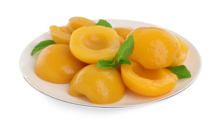 Photo of Plate with canned peach halves and mint leaves isolated on white