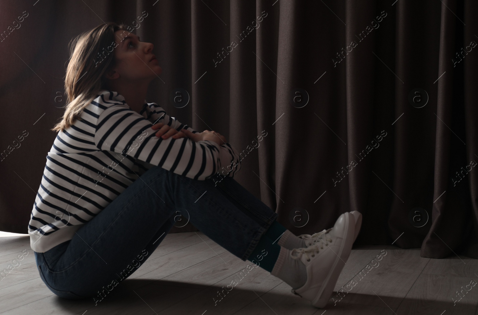 Photo of Sad young woman sitting on floor indoors, space for text