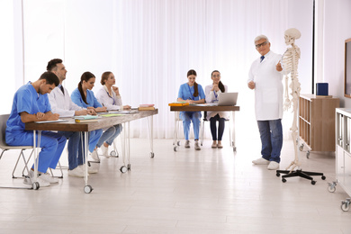 Medical students and professor studying human skeleton anatomy in classroom