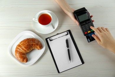 Woman with credit card using modern payment terminal at white table, top view