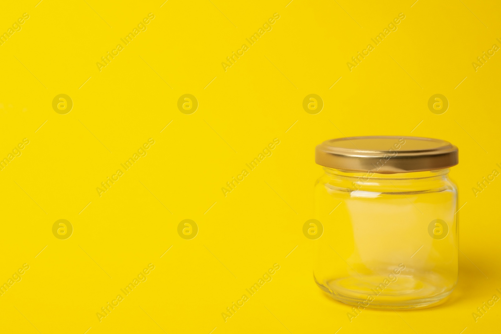 Photo of Closed empty glass jar on yellow background, space for text