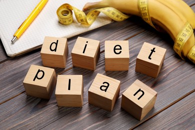 Phrase Diet Plan made of cubes, measuring tape and bananas on grey wooden table. Weight loss program