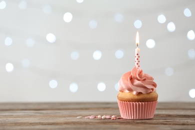 Delicious birthday cupcake with burning candle and space for text on blurred lights background