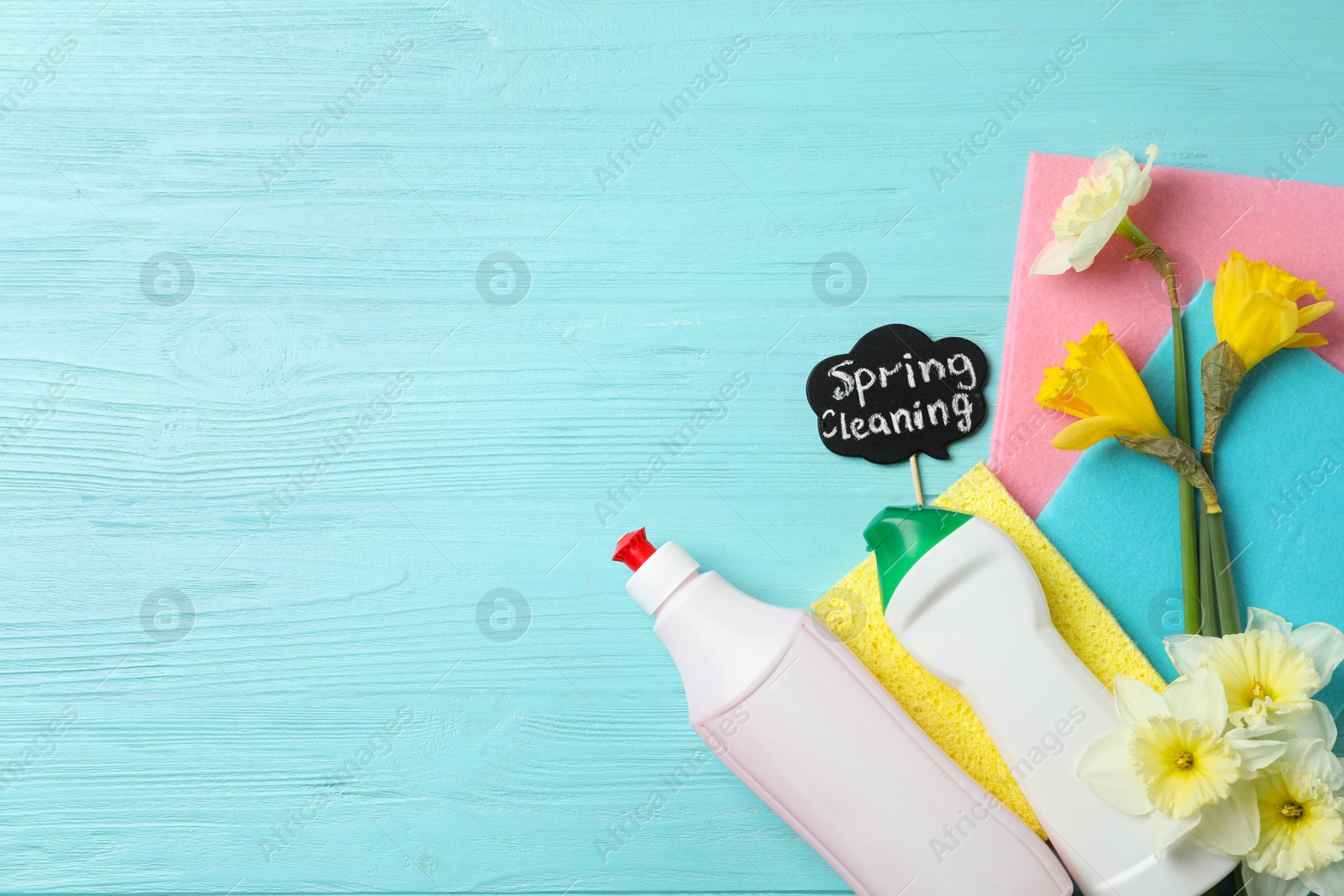 Photo of Composition with Spring Cleaning sign, flowers and detergents on light blue wooden table, flat lay. Space for text