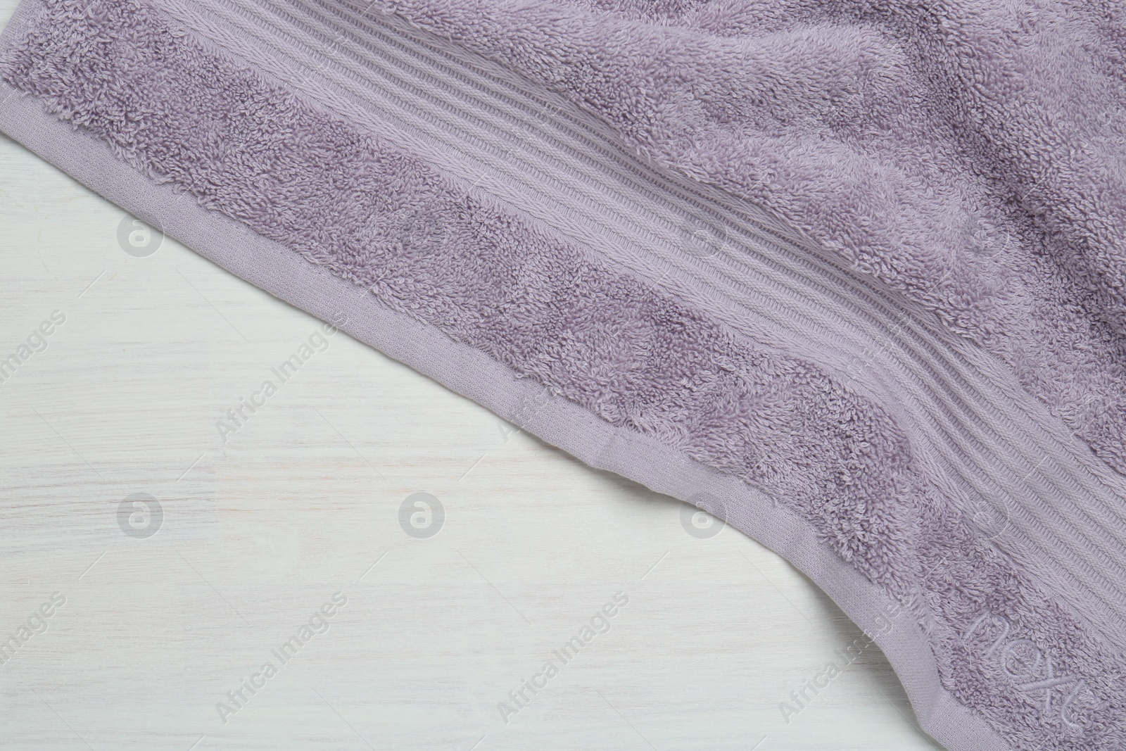 Photo of Violet terry towel on light wooden table, top view. Space for text