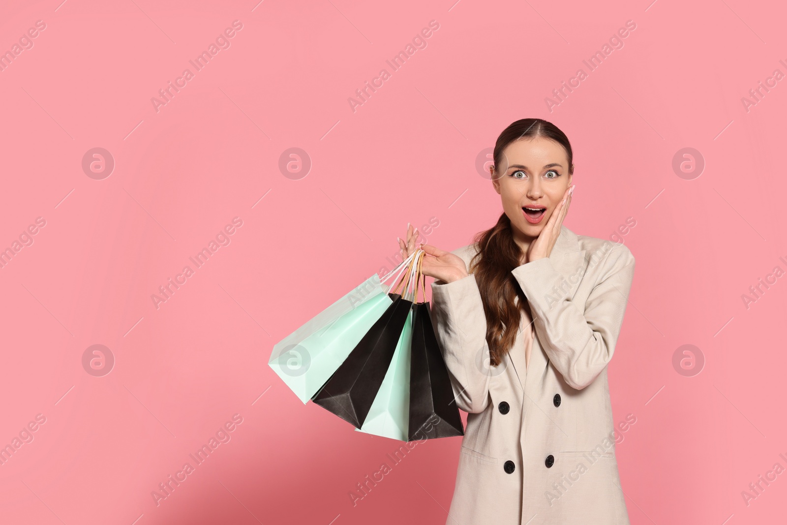 Photo of Excited young woman with shopping bags on pink background, space for text