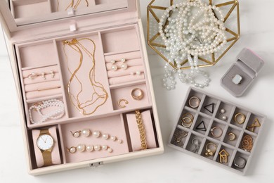 Jewelry boxes with many different accessories on white marble table, flat lay