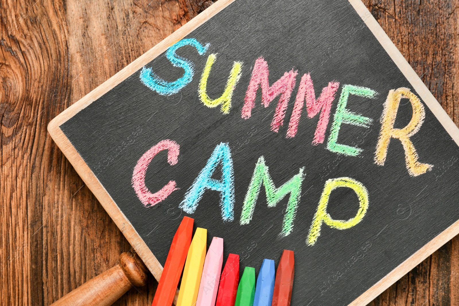 Photo of Little blackboard with text SUMMER CAMP chalked in different colors on table, top view