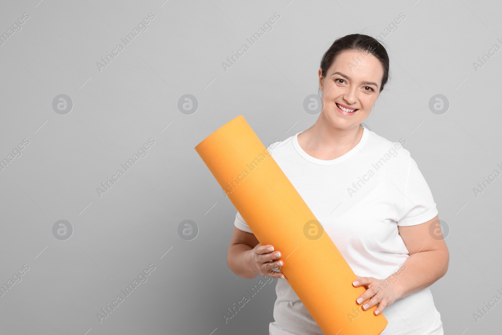 Photo of Happy overweight woman with yoga mat on grey background, space for text