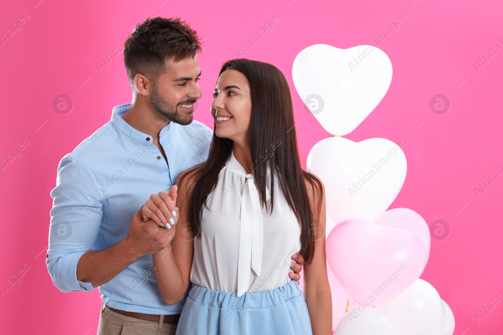 Photo of Young couple and air balloons on pink background. Celebration of Saint Valentine's Day