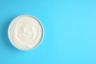 Bowl of sour cream on light blue background, top view. Space for text