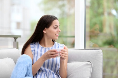 Photo of Young beautiful woman drinking morning coffee near window at home