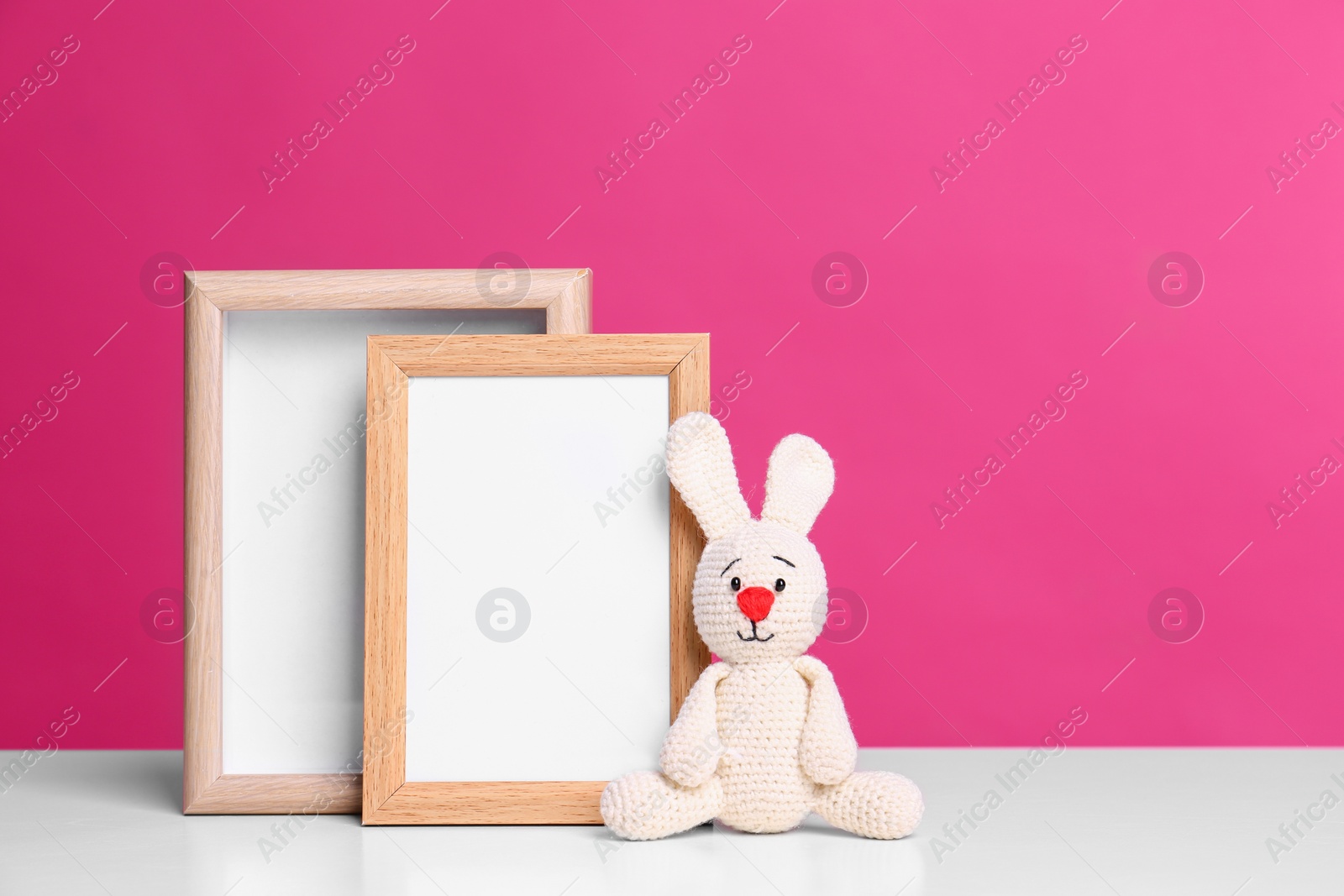 Photo of Photo frames and adorable toy bunny on table against color background, space for text. Child room elements