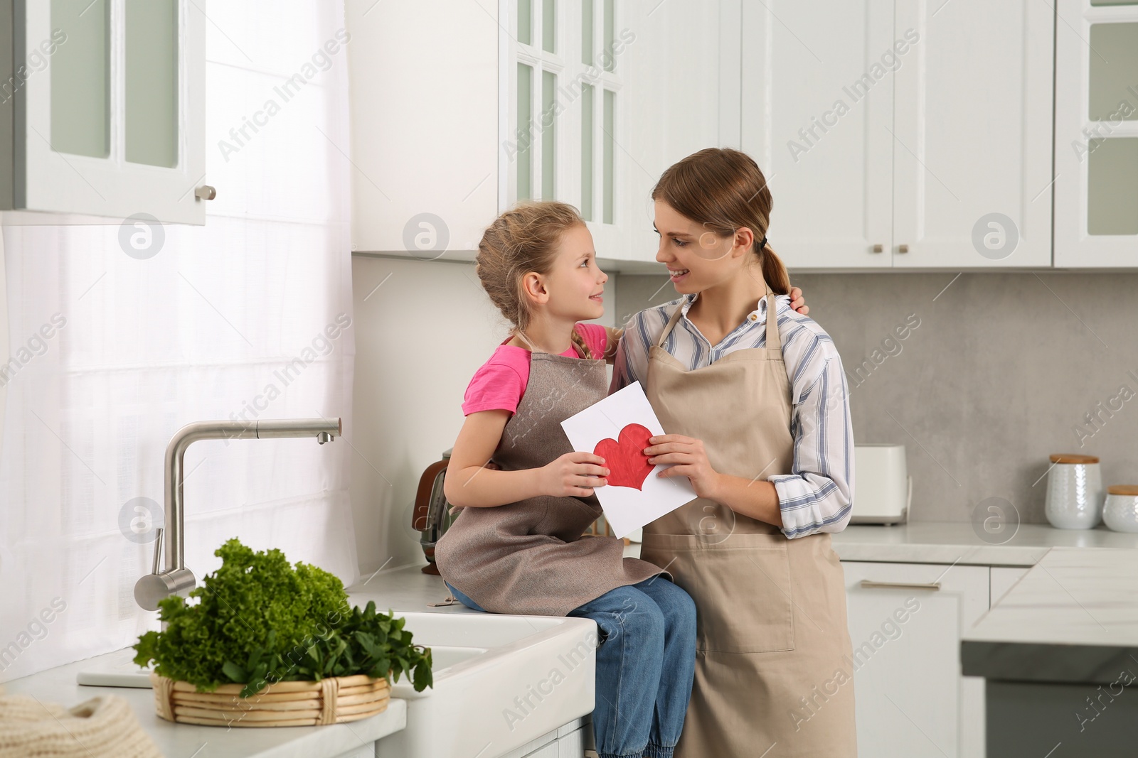 Photo of Little daughter congratulating mom with greeting card in kitchen. Happy Mother's Day