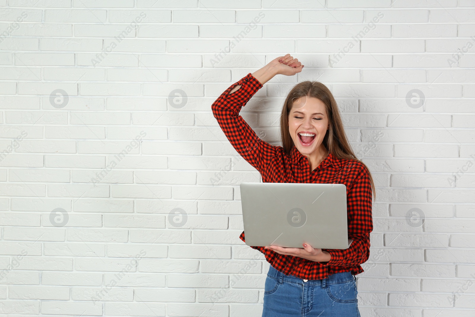 Photo of Emotional young woman with laptop celebrating victory near brick wall. Space for text