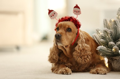 Photo of Adorable Cocker Spaniel dog in Santa headband near decorative Christmas tree, space for text