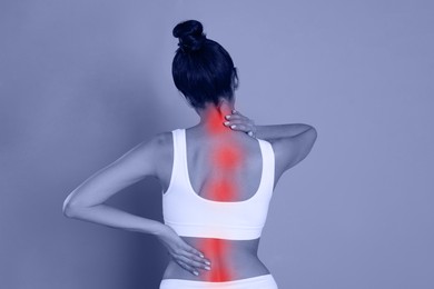 Woman suffering from back pain on color background